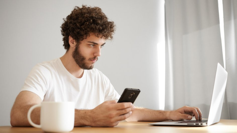 Мужчина сидит за столом с ноутбуком и телефоном и создает домовой чат