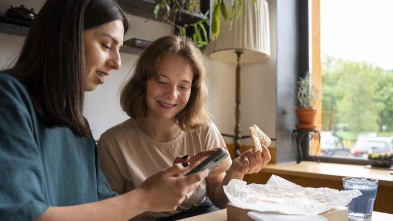 Девушки за столом с едой читают с телефона правила общения в домовом чате